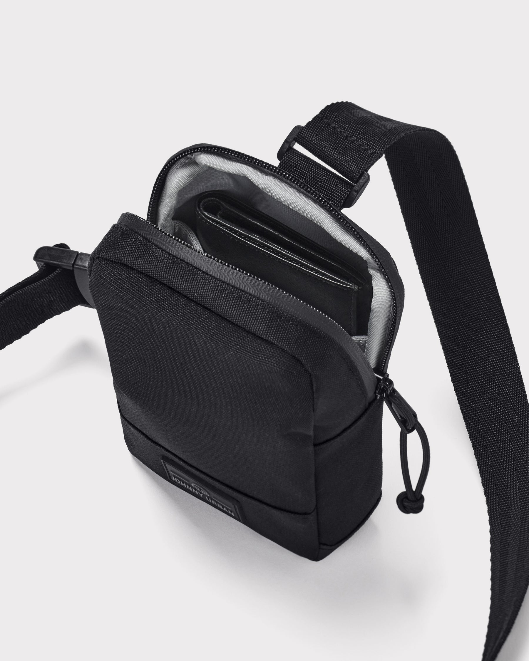 Schwarze Brusttasche 'Arthur' von Johnny Urban mit Reißverschluss geöffnet, darin ein Portemonnaie