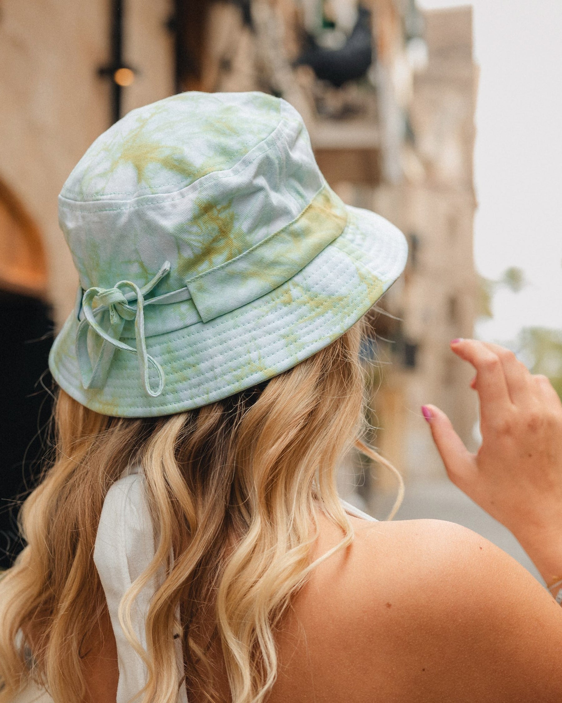 Frau trägt Bucket Hat 'Gill' von Johnny Urban in pastellfarbenem Batikmuster, Rückansicht in urbaner Umgebung
