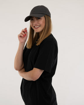 Frau trägt dunklegraue Cap 'Jen' und schwarzes T-Shirt, lächelnd, mittellange Haare