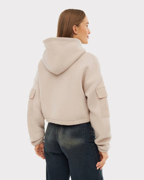 Rückansicht eines Models mit sandfarbenem, kurz geschnittenem Hoodie 'Carly' mit Kapuze und Taschen an den Ärmeln