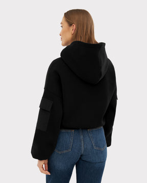 Damen trägt schwarzen Cropped Hoodie ‚Carly‘ mit Kapuze und Tasche am linken Ärmel