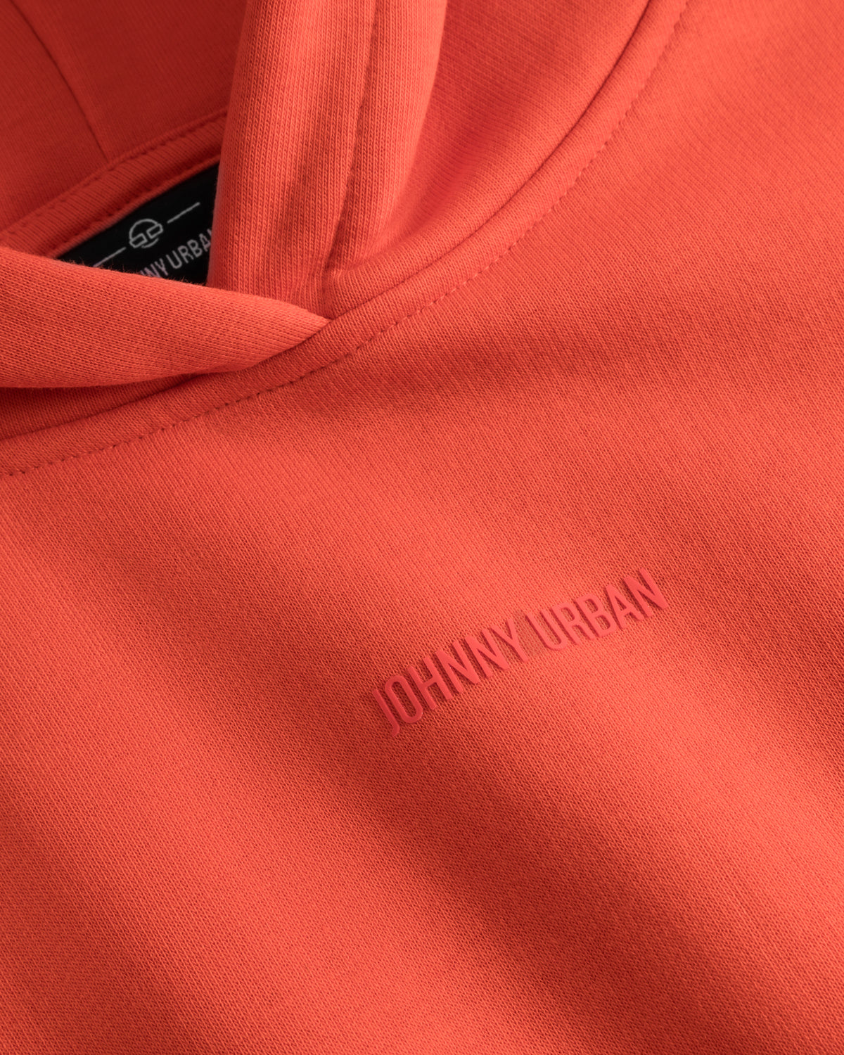 Detailaufnahme eines orangen Cropped Hoodies 'Carly' mit eingeprägtem Schriftzug 'Johnny Urban'
