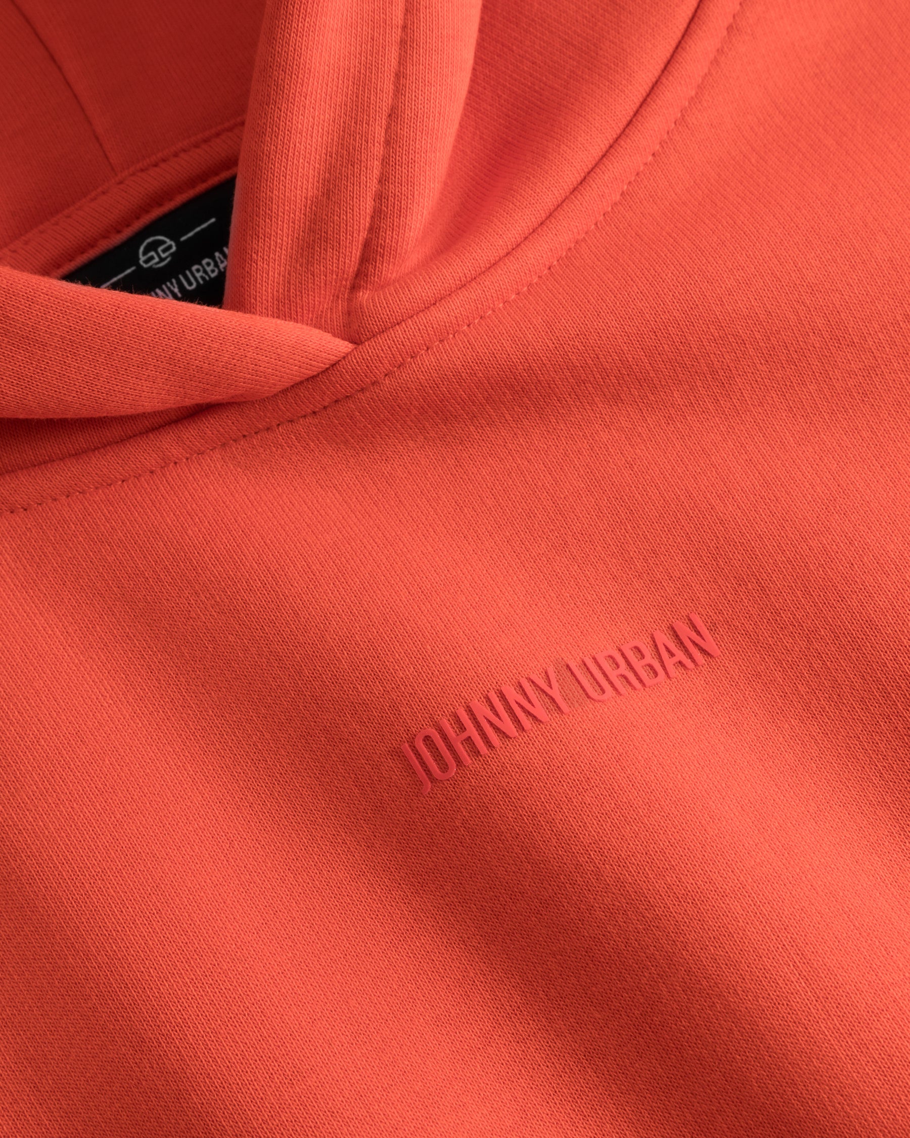 Detailaufnahme eines orangen Cropped Hoodies 'Carly' mit eingeprägtem Schriftzug 'Johnny Urban'