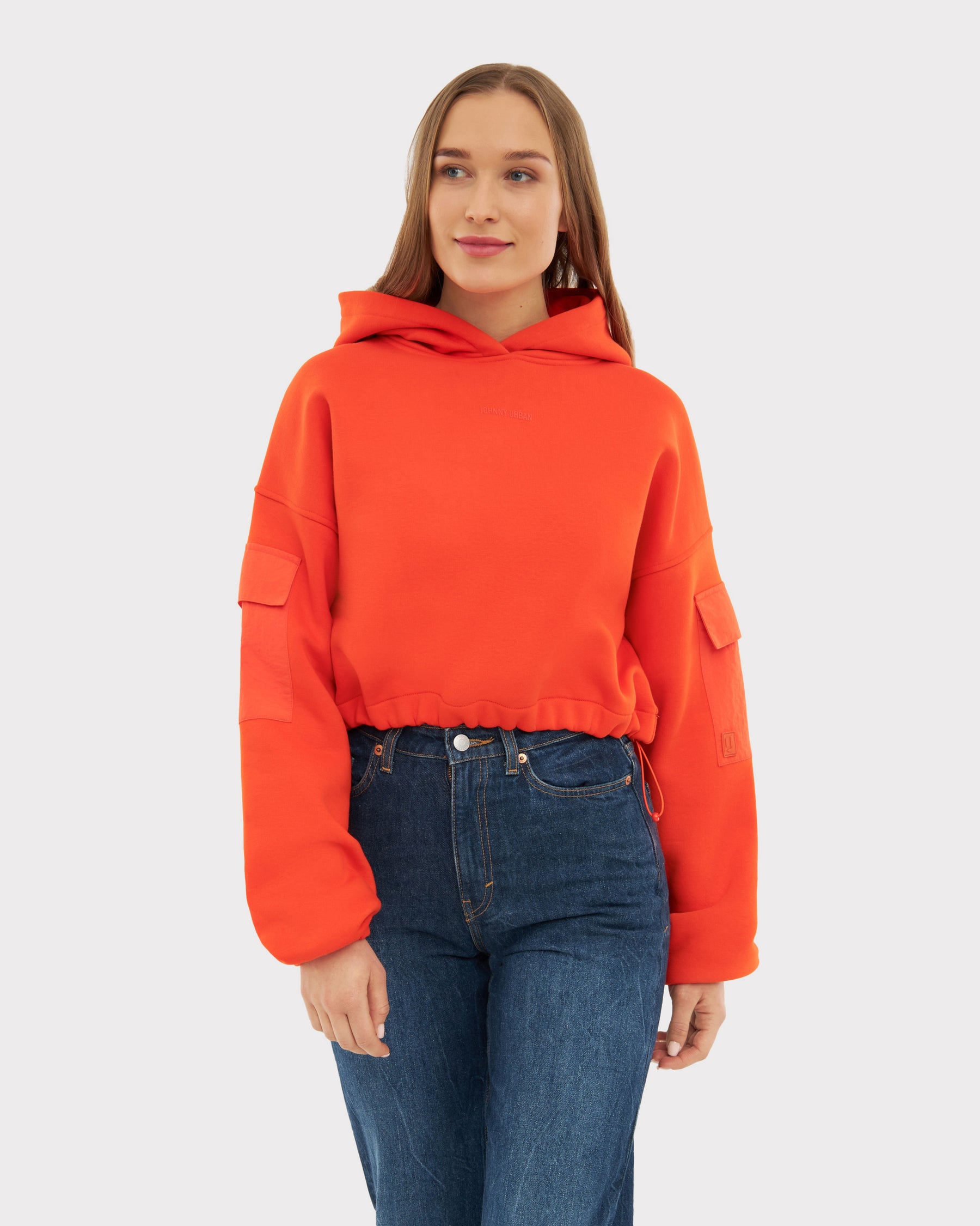 Junge Frau trägt rotes, kurzes Hoodie 'Carly' mit Taschen an den Ärmeln und blauen Jeans