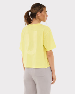 Frau trägt gelbes Cropped T-Shirt 'Zoey JU' und graue Hose, Rückansicht