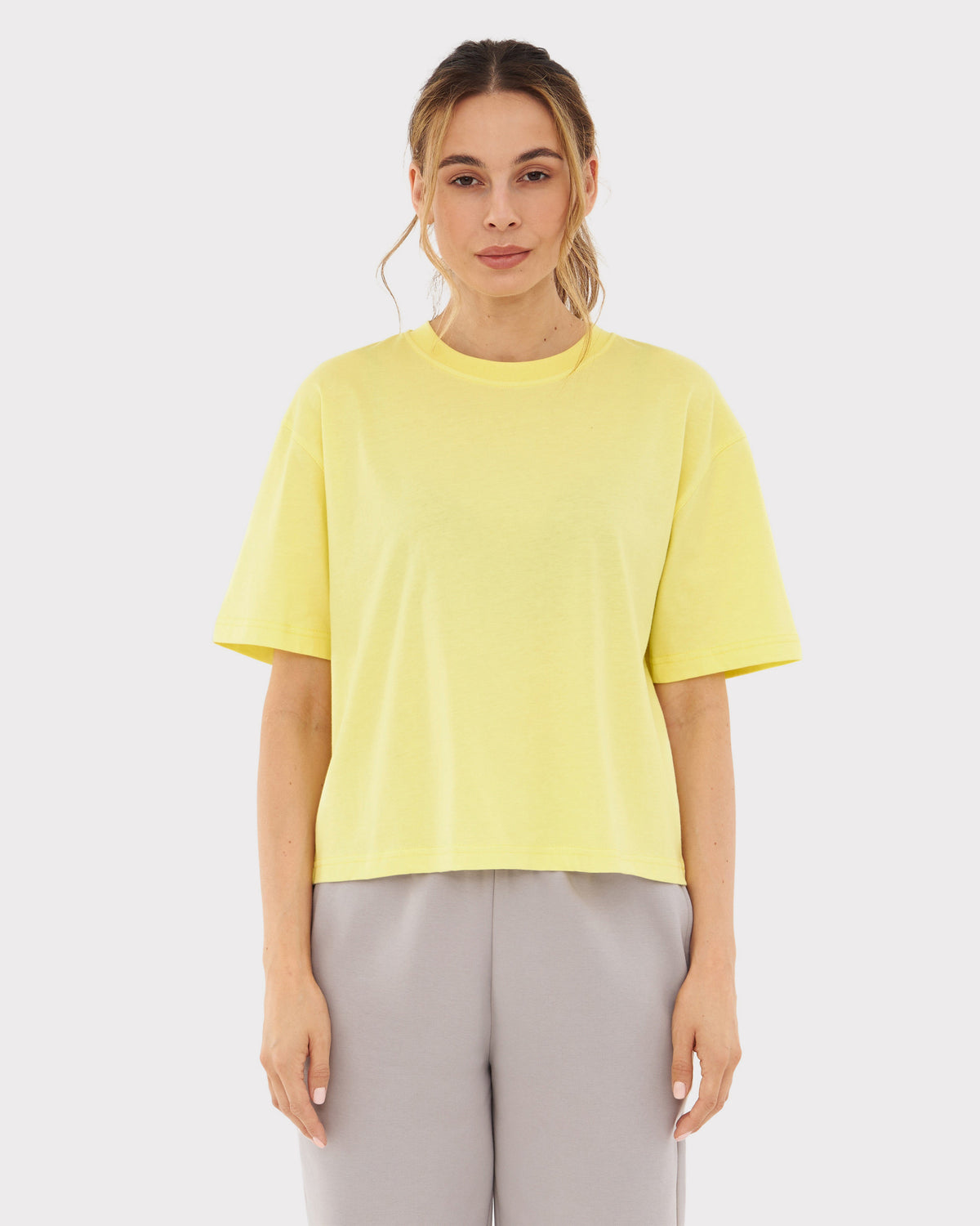 Frau trägt gelbes Cropped T-Shirt 'Zoey JU' und graue Hose, frontal stehend
