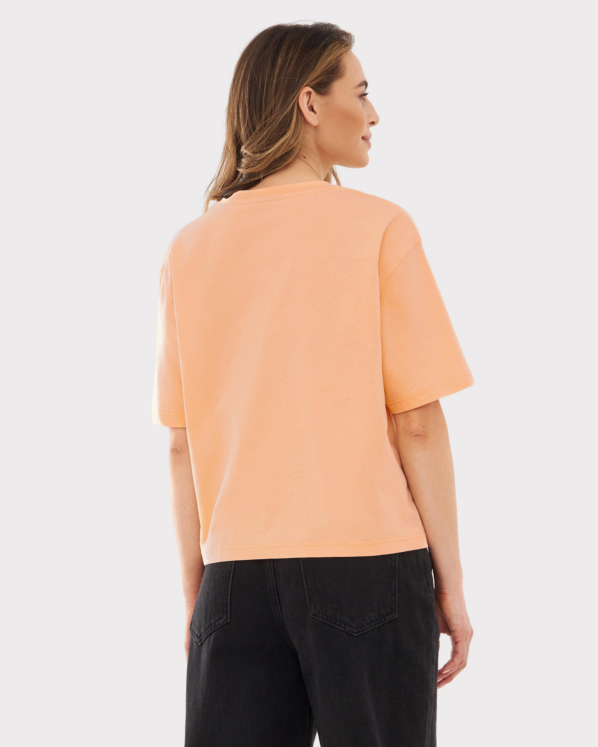 Rückansicht einer Frau mit peachfarbenem, oversized Cropped T-Shirt 'Zoey' und schwarzen Jeans