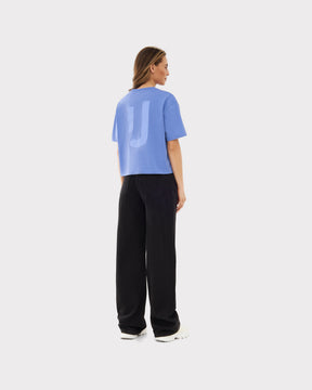 Rückansicht einer Frau mit blauer Cropped T-Shirt 'Zoey JU' und schwarzen weiten Hosen