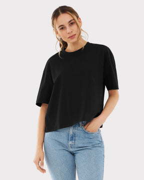 Frau trägt schwarzes Cropped T-Shirt 'Zoey' mit asymmetrischem Saum und hellblauen Jeans