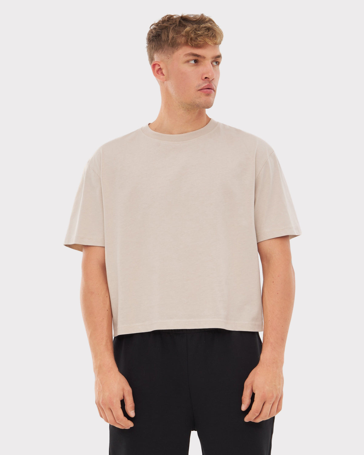 Mann trägt beige Cropped T-Shirt 'Zoey' mit kurzen Ärmeln und schwarzen Hosen