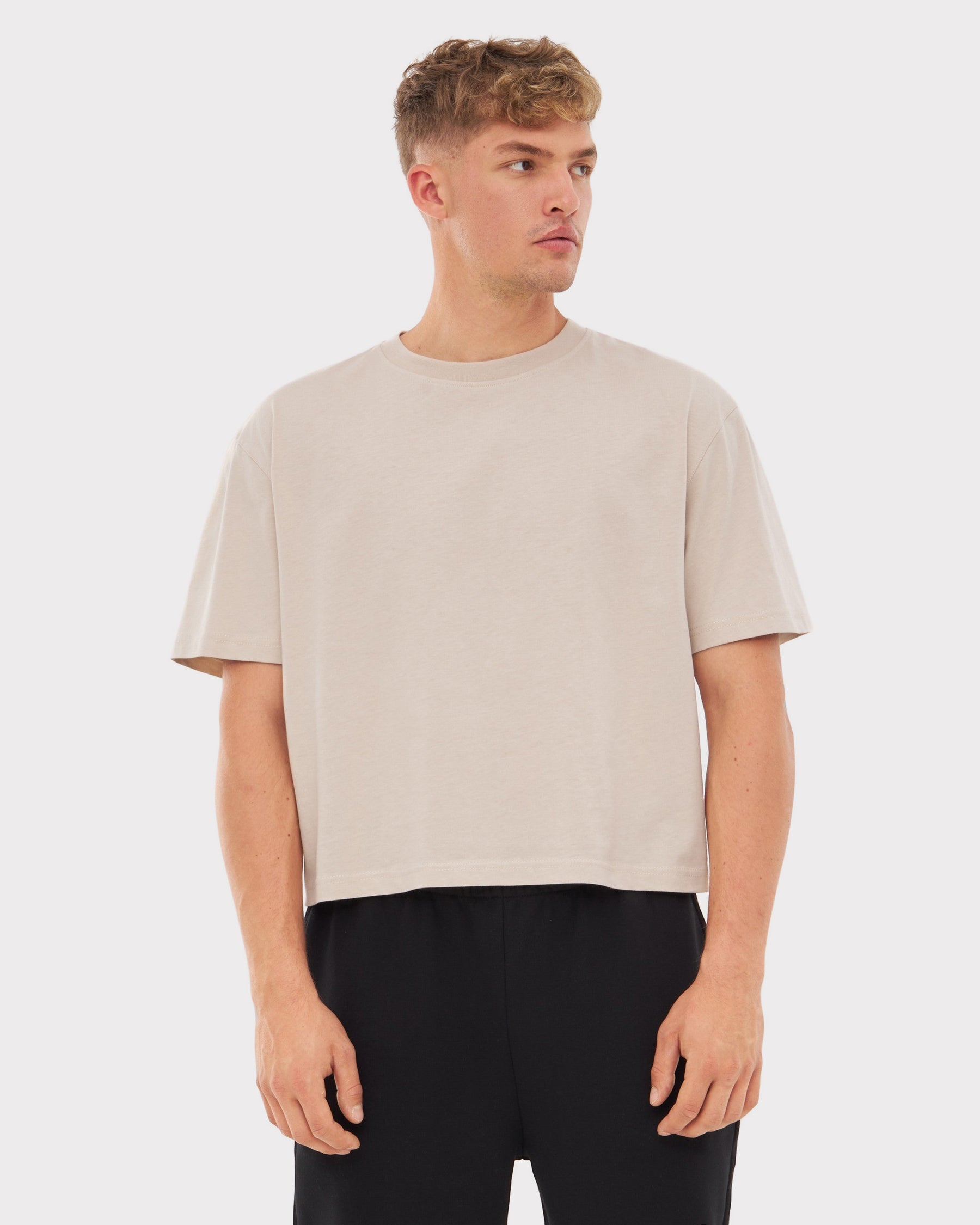 Mann trägt beige Cropped T-Shirt 'Zoey' mit kurzen Ärmeln und schwarzen Hosen