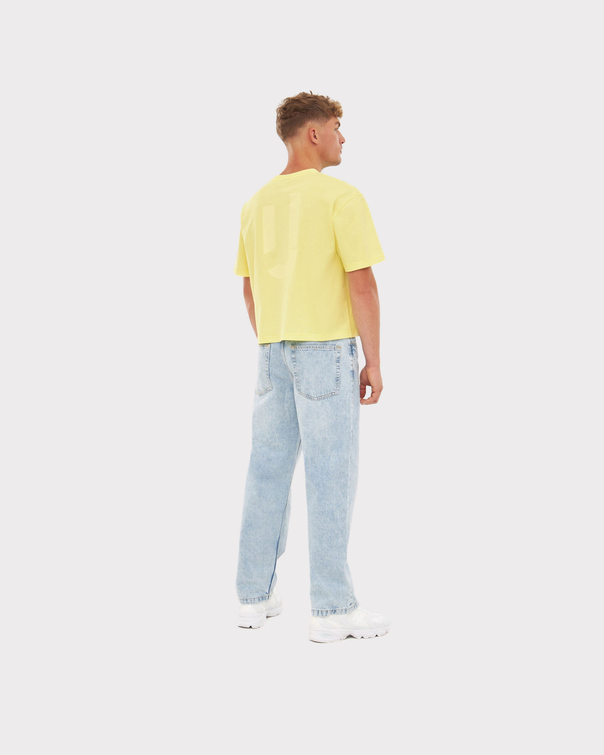 Mann trägt gelbes Cropped T-Shirt 'Zoey JU' und helle weite Jeans von hinten