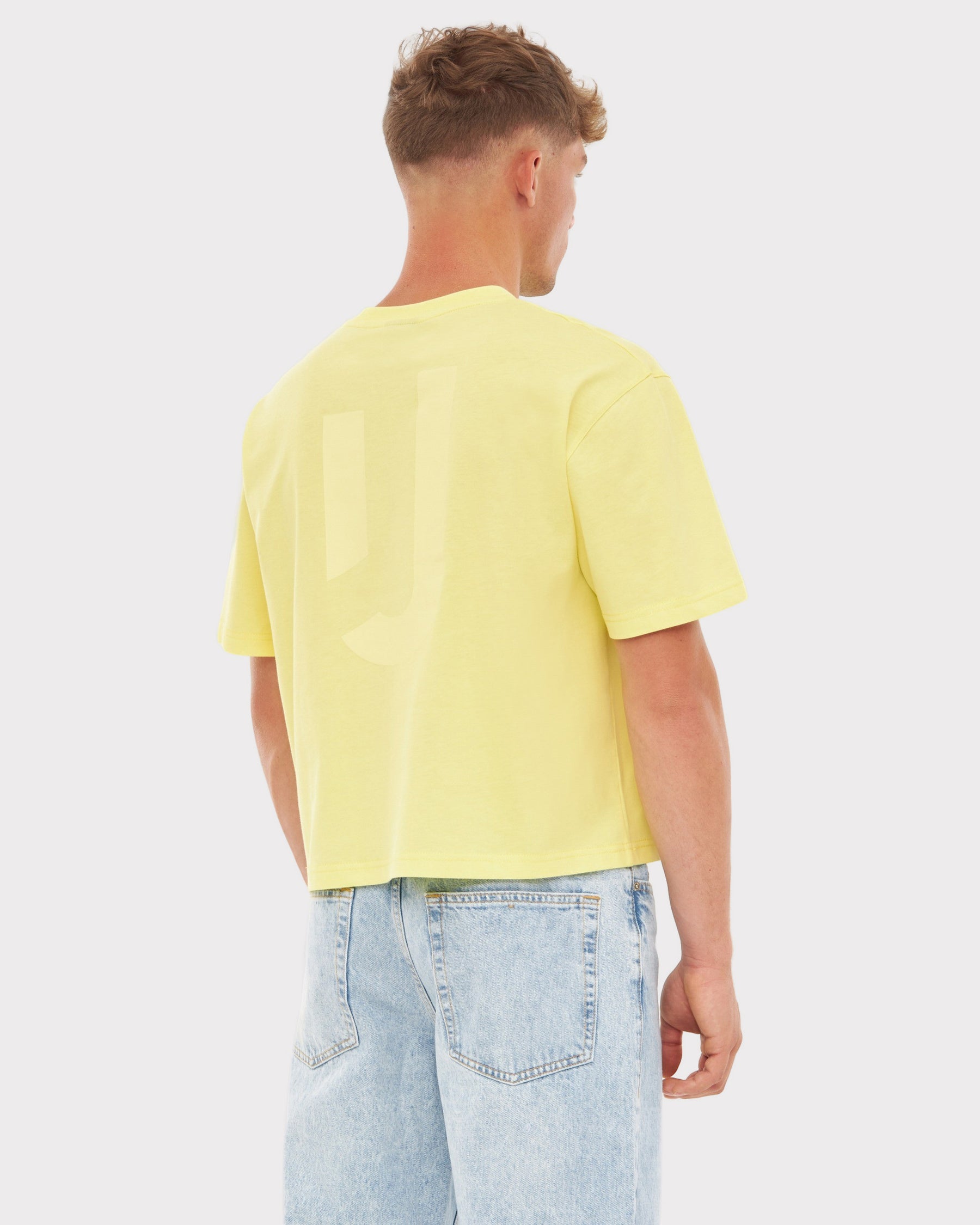 Männliches Modell trägt gelbes Cropped T-Shirt 'Zoey JU' von hinten mit hellblauen Jeans