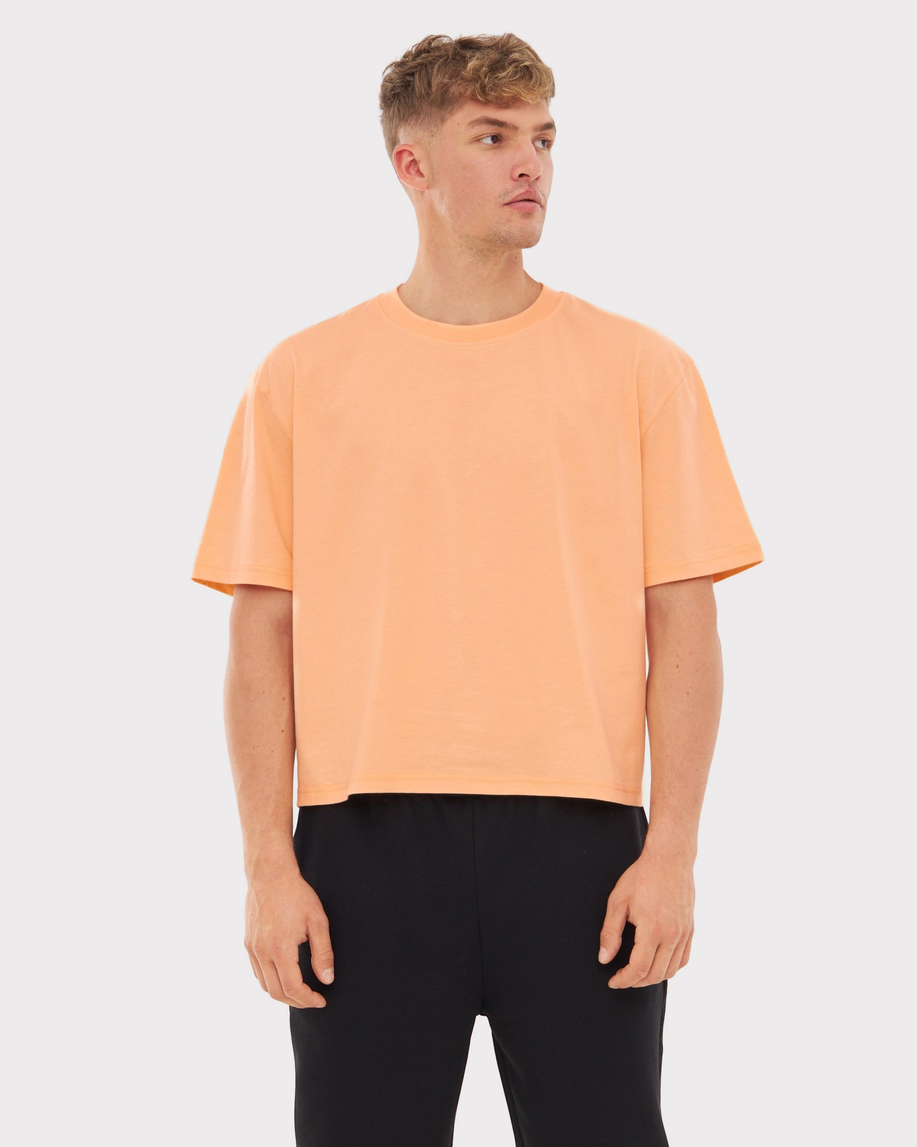 Mann trägt Cropped T-Shirt 'Zoey' in Pfirsichfarbe mit kurzen Ärmeln und rundem Ausschnitt
