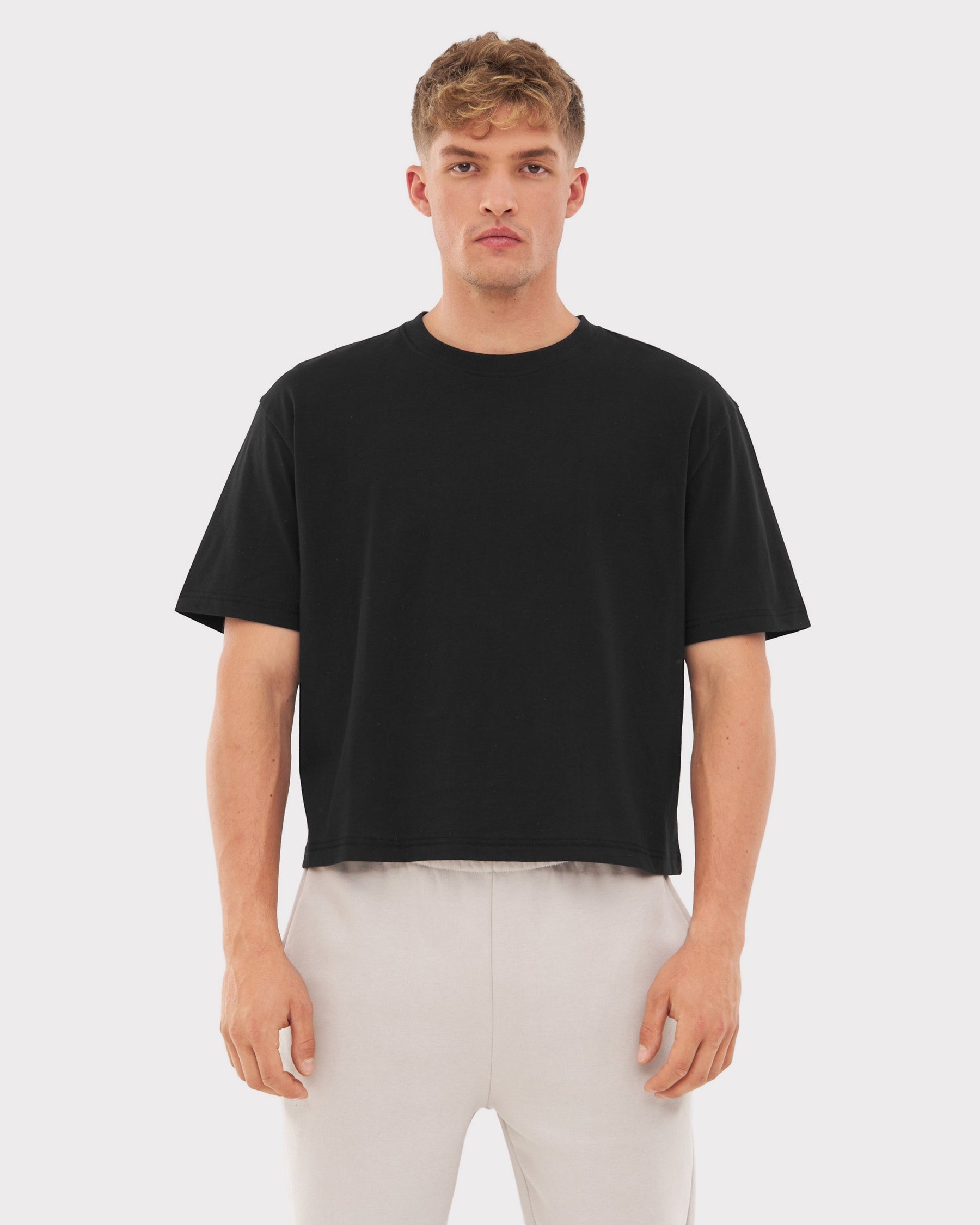 Mann trägt schwarzes Cropped T-Shirt 'Zoey' und helle Hose