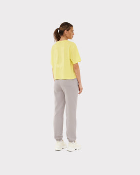 Frau von hinten in gelbem Cropped T-Shirt 'Zoey JU' und hellgrauen Jogginghosen mit weißen Sneakern