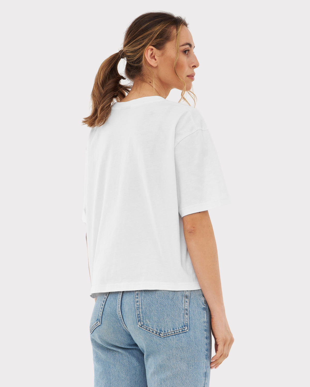 Frau trägt weiße oversized Cropped T-Shirt 'Zoey' und blaue Jeans, Rückansicht