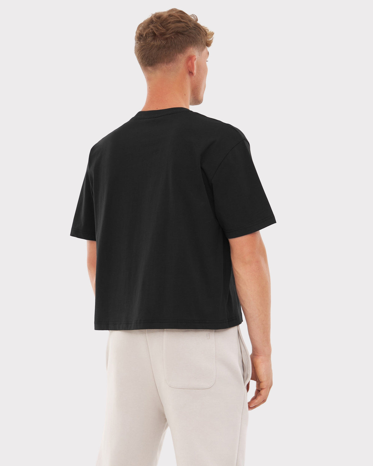 Mann von hinten trägt schwarzes Oversize Cropped T-Shirt 'Zoey' und helle Hose