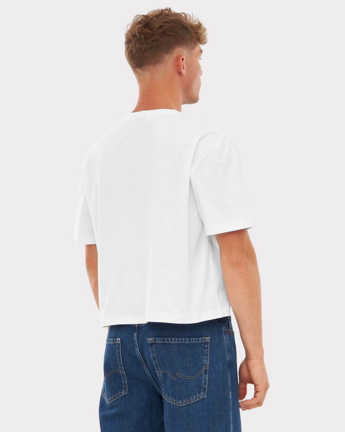 Mann trägt weißes oversize Cropped T-Shirt 'Zoey' von hinten, kombiniert mit blauen Jeans
