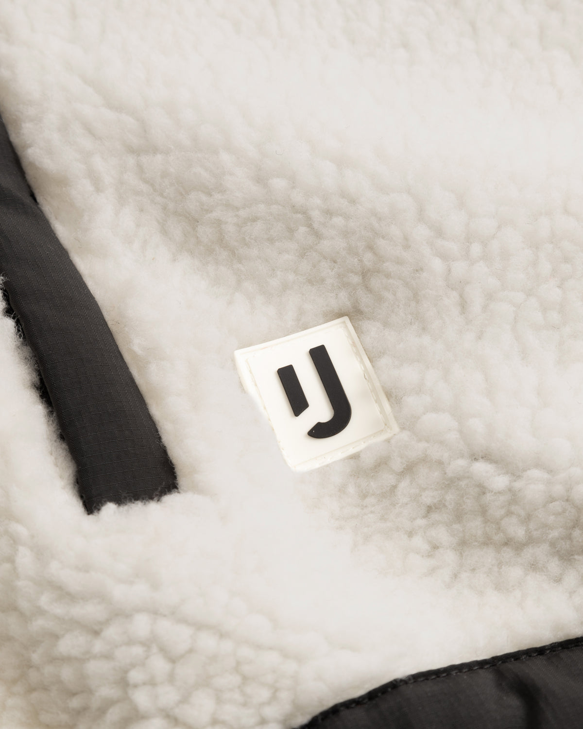 Nahaufnahme der cremefarbenen Cropped Teddy Fleecejacke 'Carey' mit Johnny Urban Logo und schwarzem Besatz