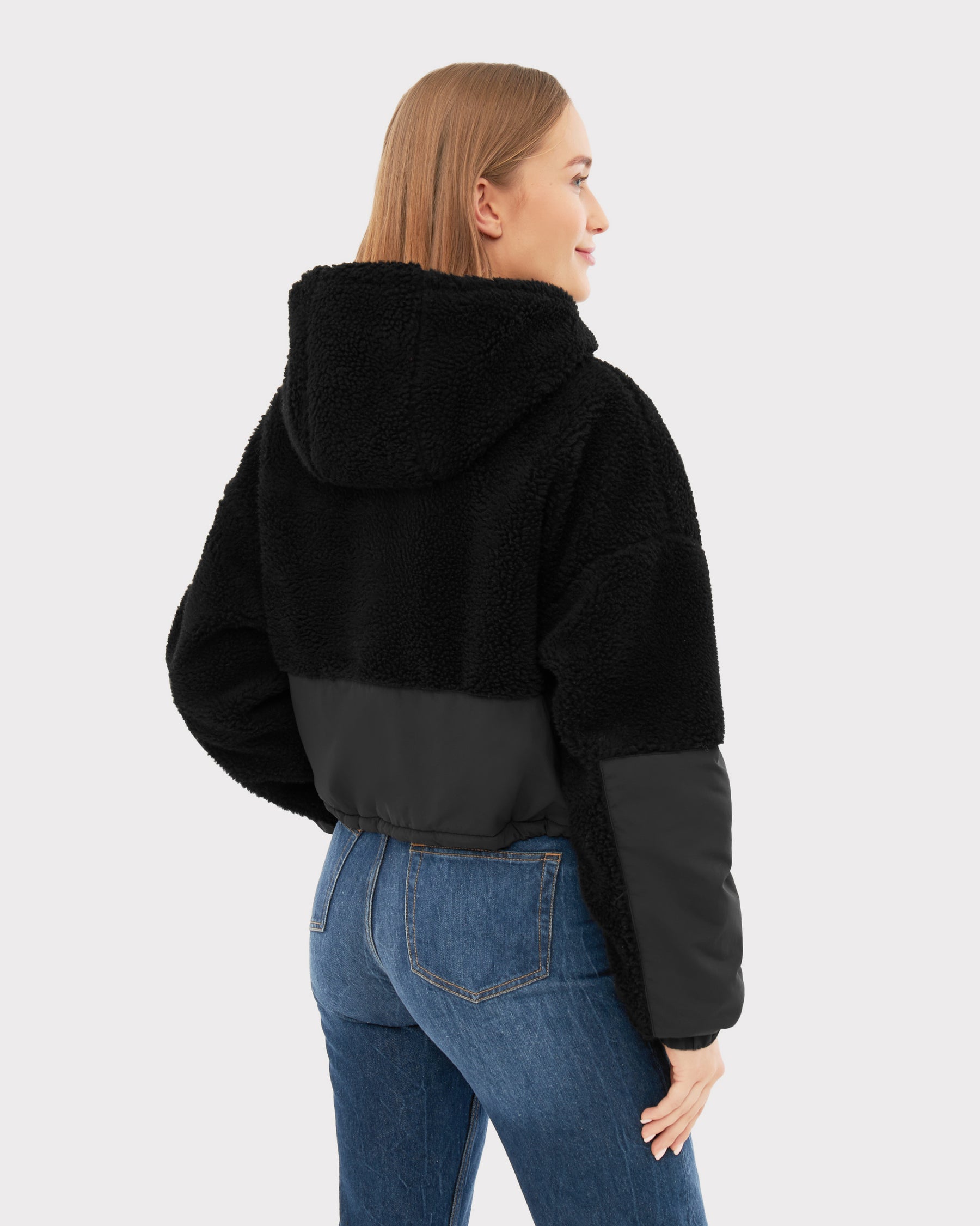 Rückansicht einer Frau in schwarzer Cropped Teddy Fleecejacke 'Carey' mit Kapuze und blauer Jeans