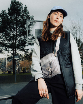 Frau mit Baseballmütze und schwarzer Nike-Weste trägt beige Umhängetasche 'Jayden' an einer urbanen Basketballanlage