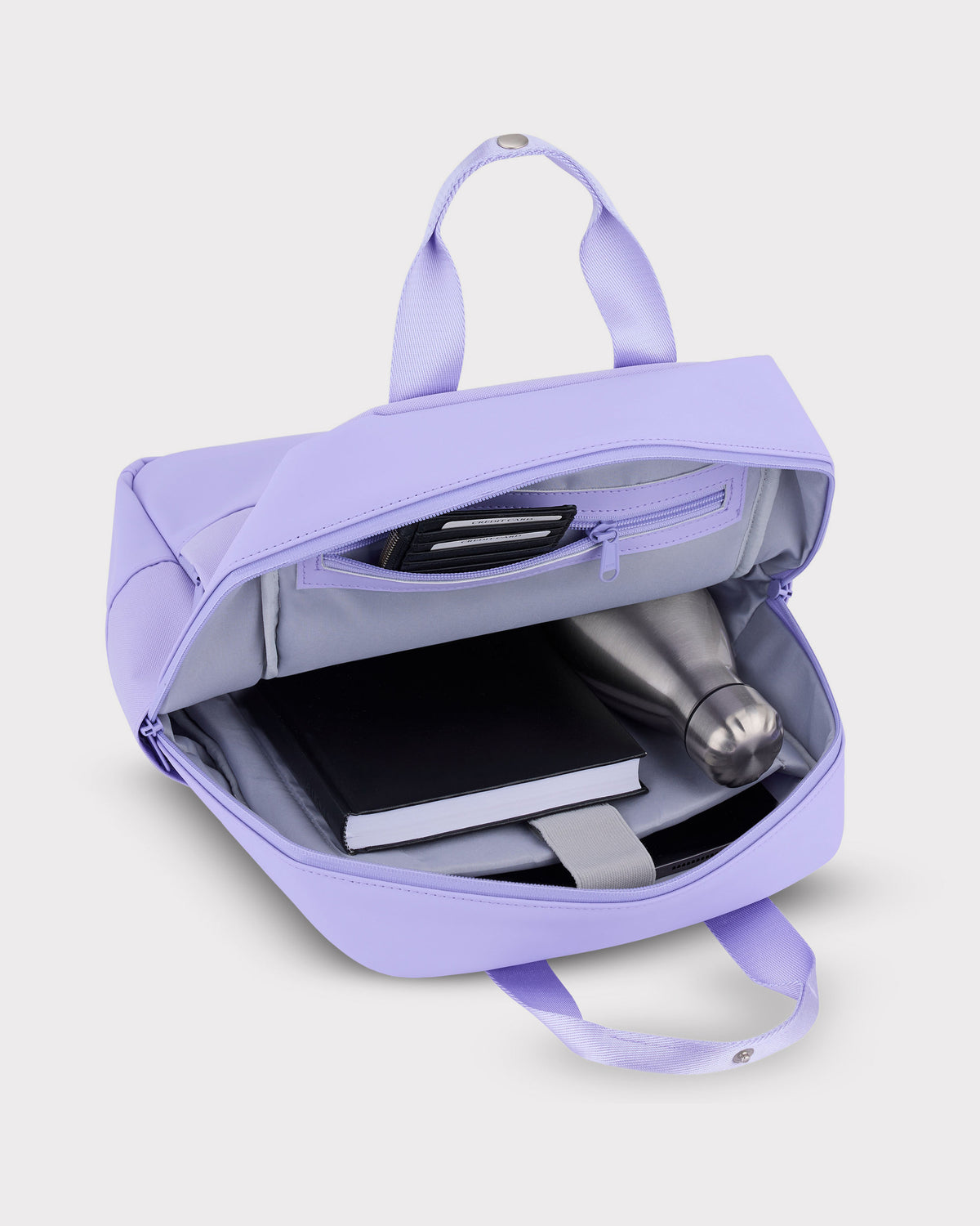 Lilafarbener Damenrucksack 'Jona Medium' geöffnet mit Buch, Wasserflasche und Kartenfächern im Innenraum