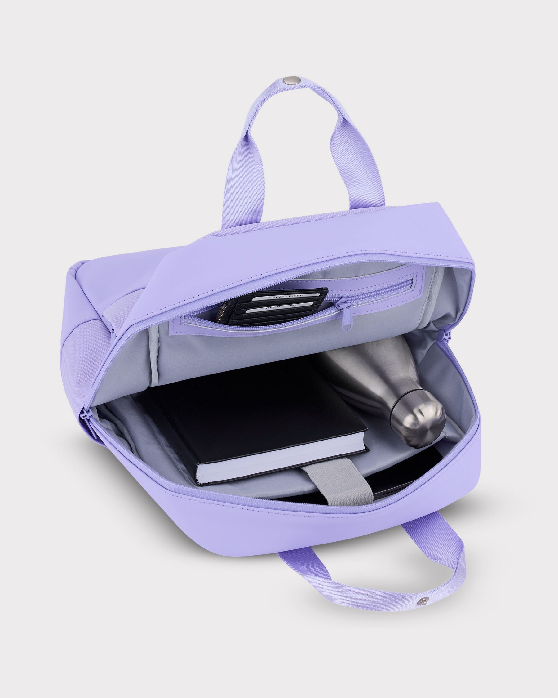 Lilafarbener Damenrucksack 'Jona Medium' geöffnet mit Buch, Wasserflasche und Kartenfächern im Innenraum