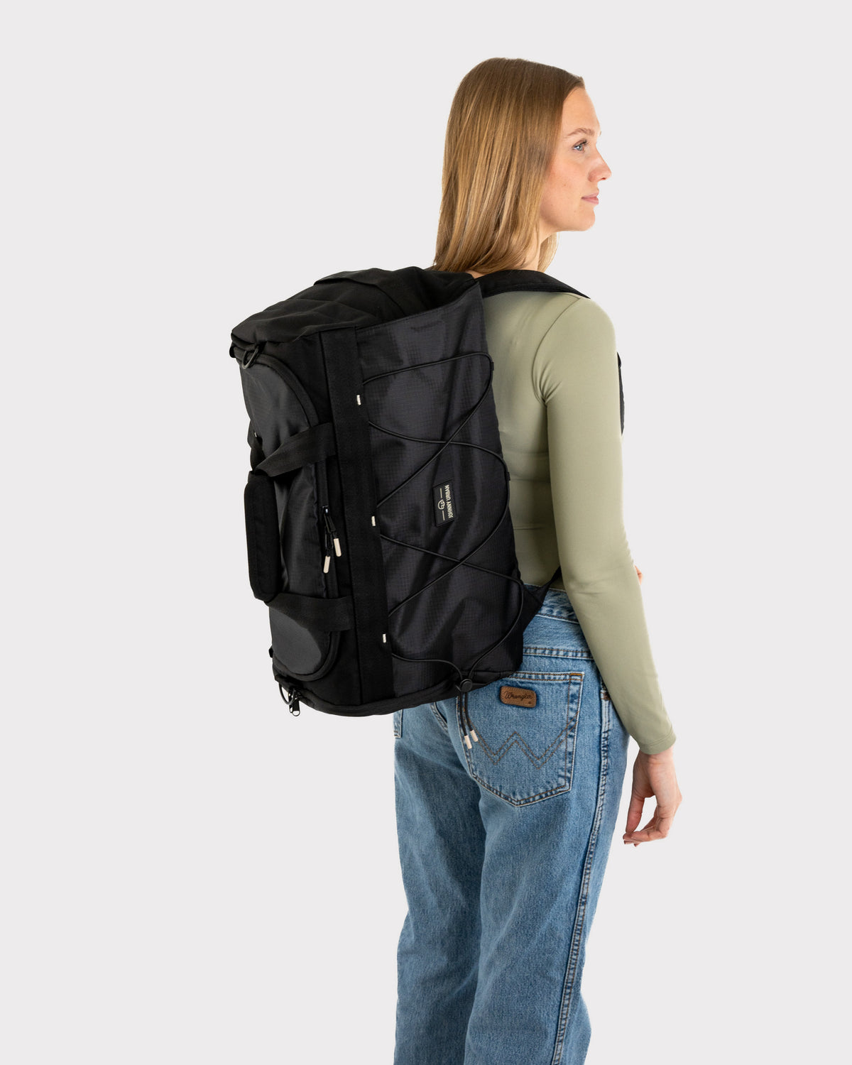 Frau trägt schwarzen Duffle Bag 'Shawn Medium' von Johnny Urban, kombiniert mit langärmeligem, olivgrünem Oberteil und Jeans