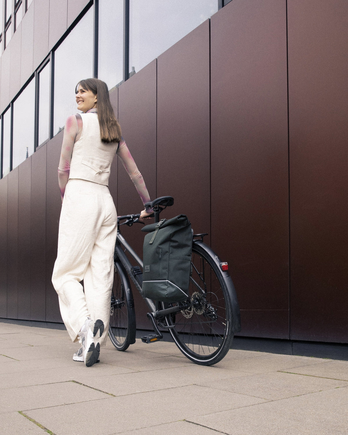 Frau schiebt Fahrrad mit dunkelgrünem Johnny Urban Rolltop Rucksack 'Robin Medium' am Gepäckträger