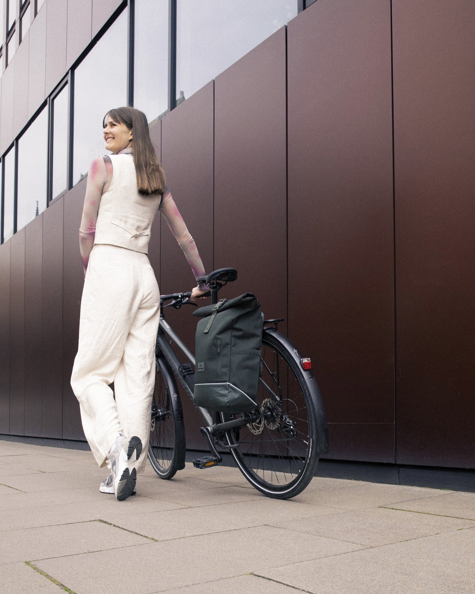 Frau schiebt Fahrrad mit dunkelgrünem Johnny Urban Rolltop Rucksack 'Robin Medium' am Gepäckträger