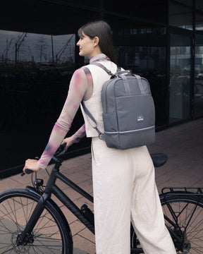 Frau mit grauem Johnny Urban Rucksack 'Jona Medium' lehnt an schwarzem Fahrrad