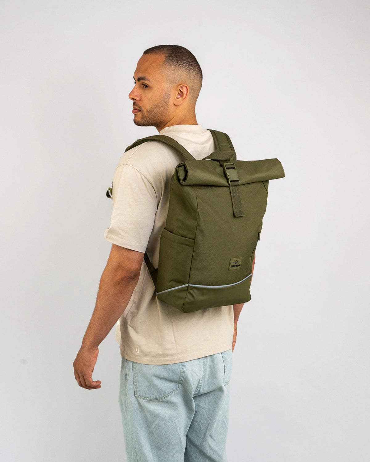 Mann trägt olivgrünen Rolltop Rucksack ‚Robin Medium‘ mit reflektierendem Streifen