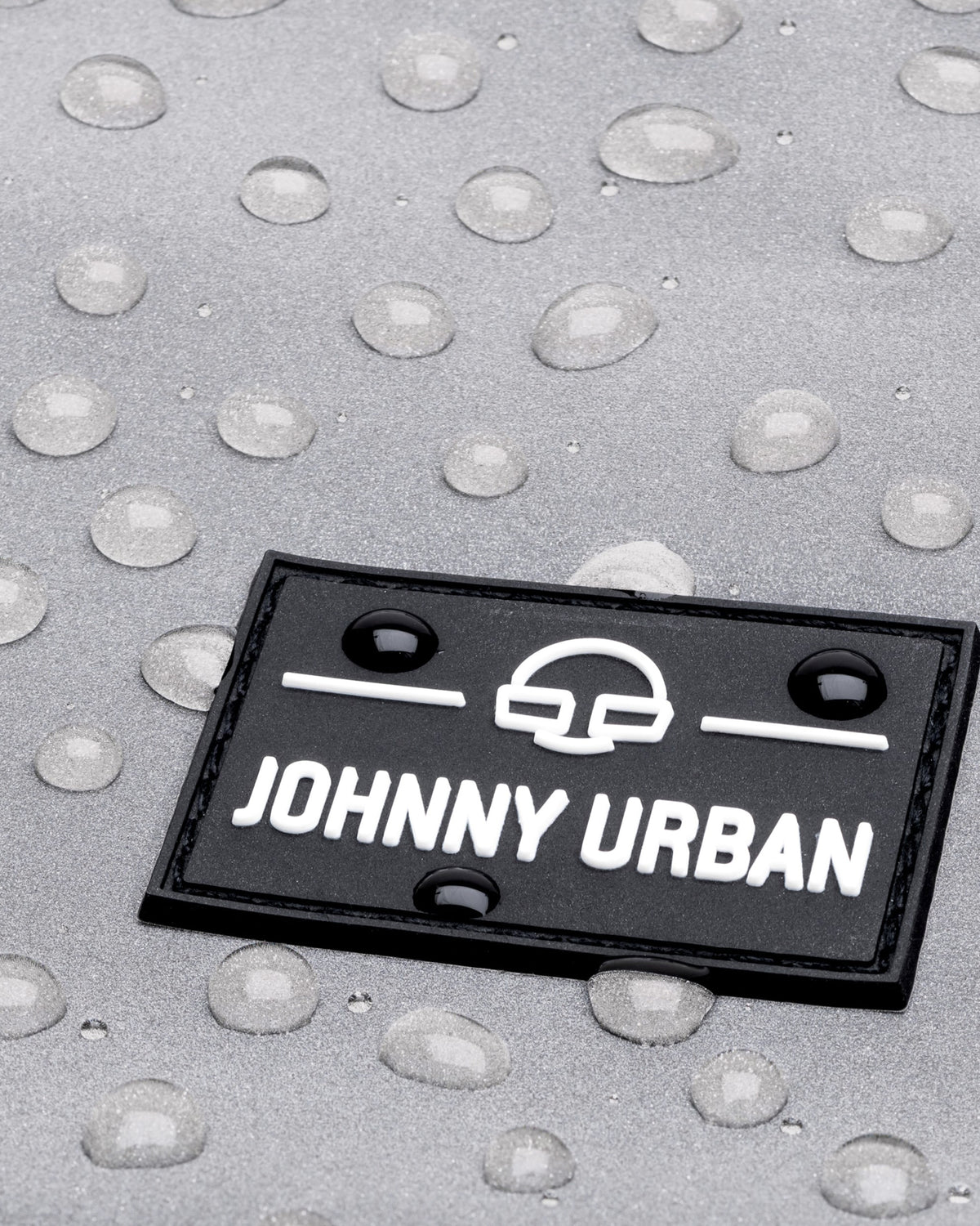 Nahaufnahme eines schwarzen Johnny Urban Logos auf silbernem, wasserabweisendem Material mit Wassertropfen