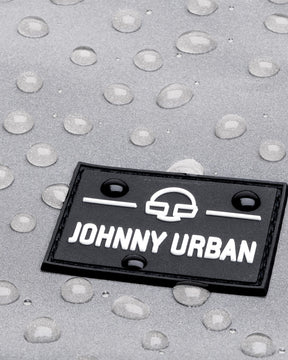 Nahaufnahme eines schwarzen Johnny Urban Logos auf silbernem, wasserabweisendem Material mit Wassertropfen