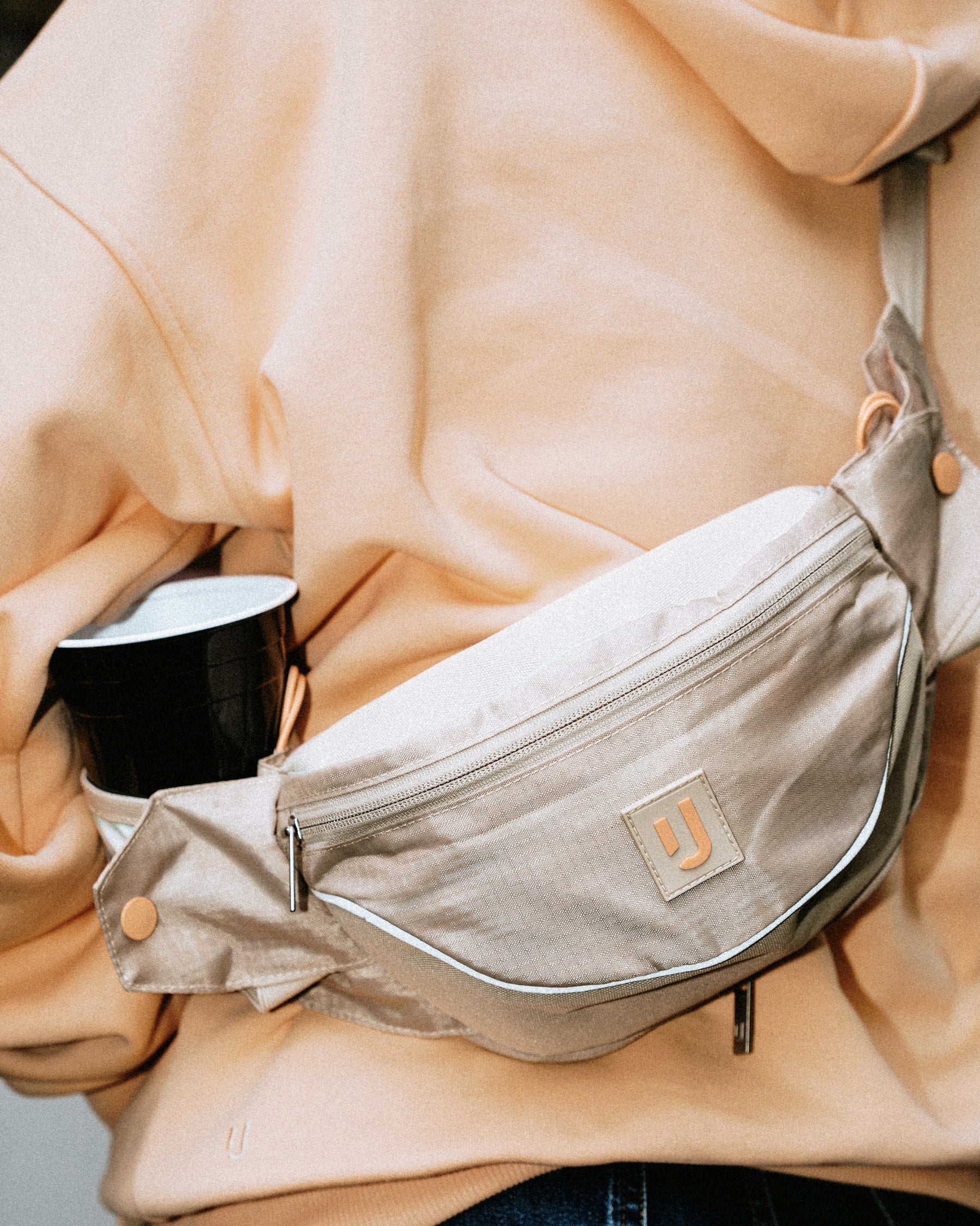 Beige 2in1 Bauchtasche 'Jimmy' von Johnny Urban mit Flaschenhalter, getragen über einem hellorangenen Hoodie