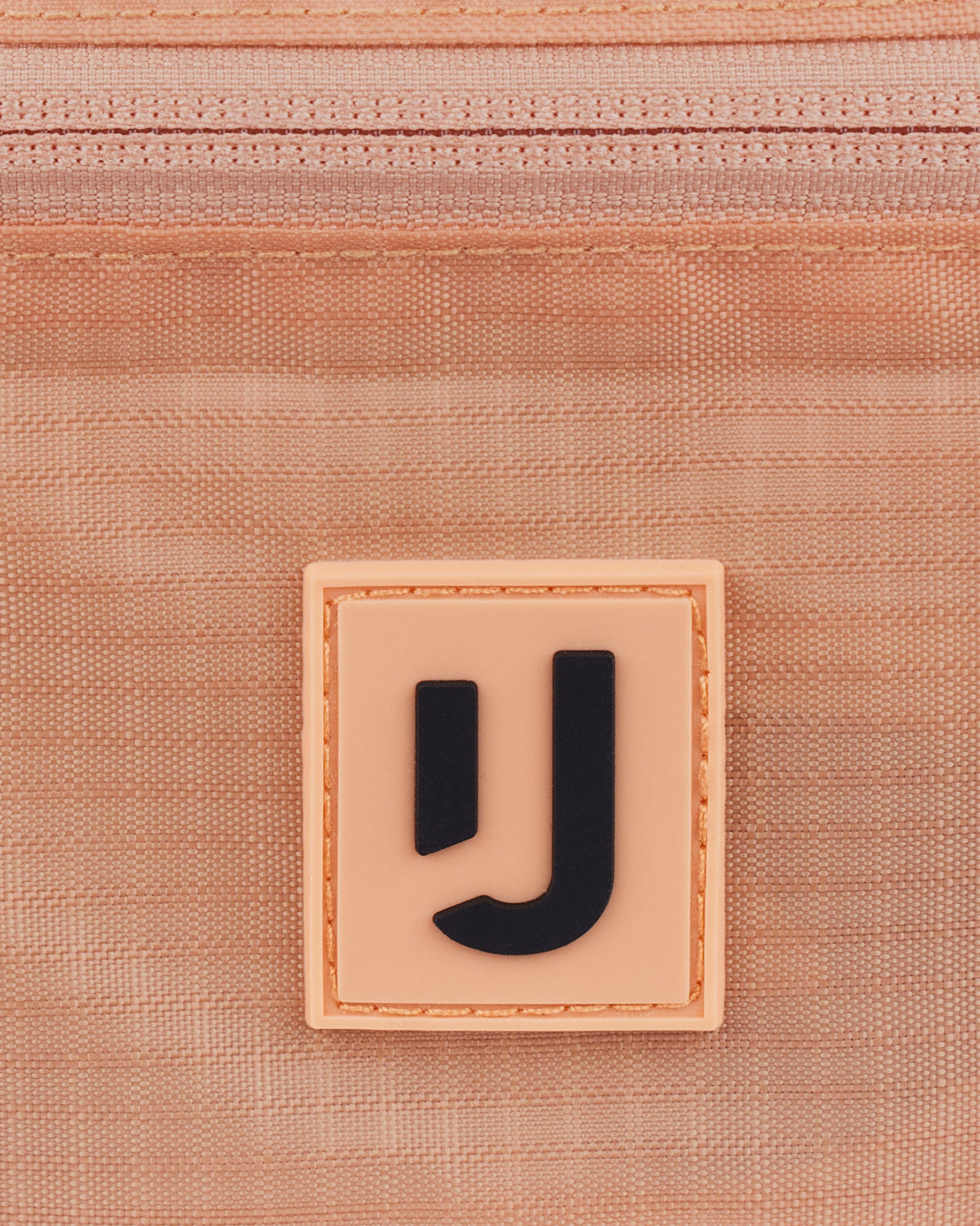 Nahe Aufnahme des Johnny Urban Logos auf der wasserabweisenden 2in1 Bauchtasche 'Jimmy' in Peach-Farbe