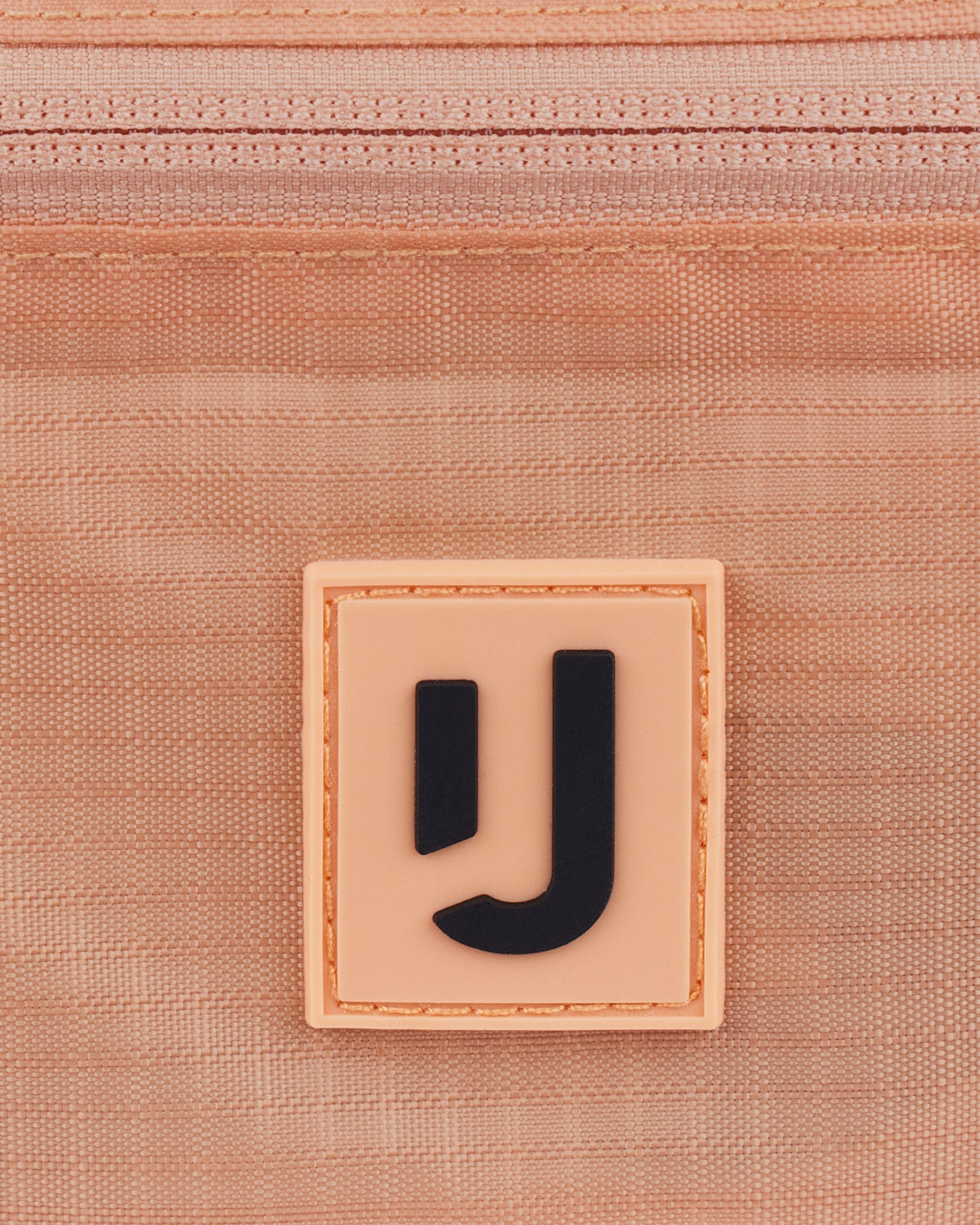 Nahe Aufnahme des Johnny Urban Logos auf der wasserabweisenden 2in1 Bauchtasche 'Jimmy' in Peach-Farbe