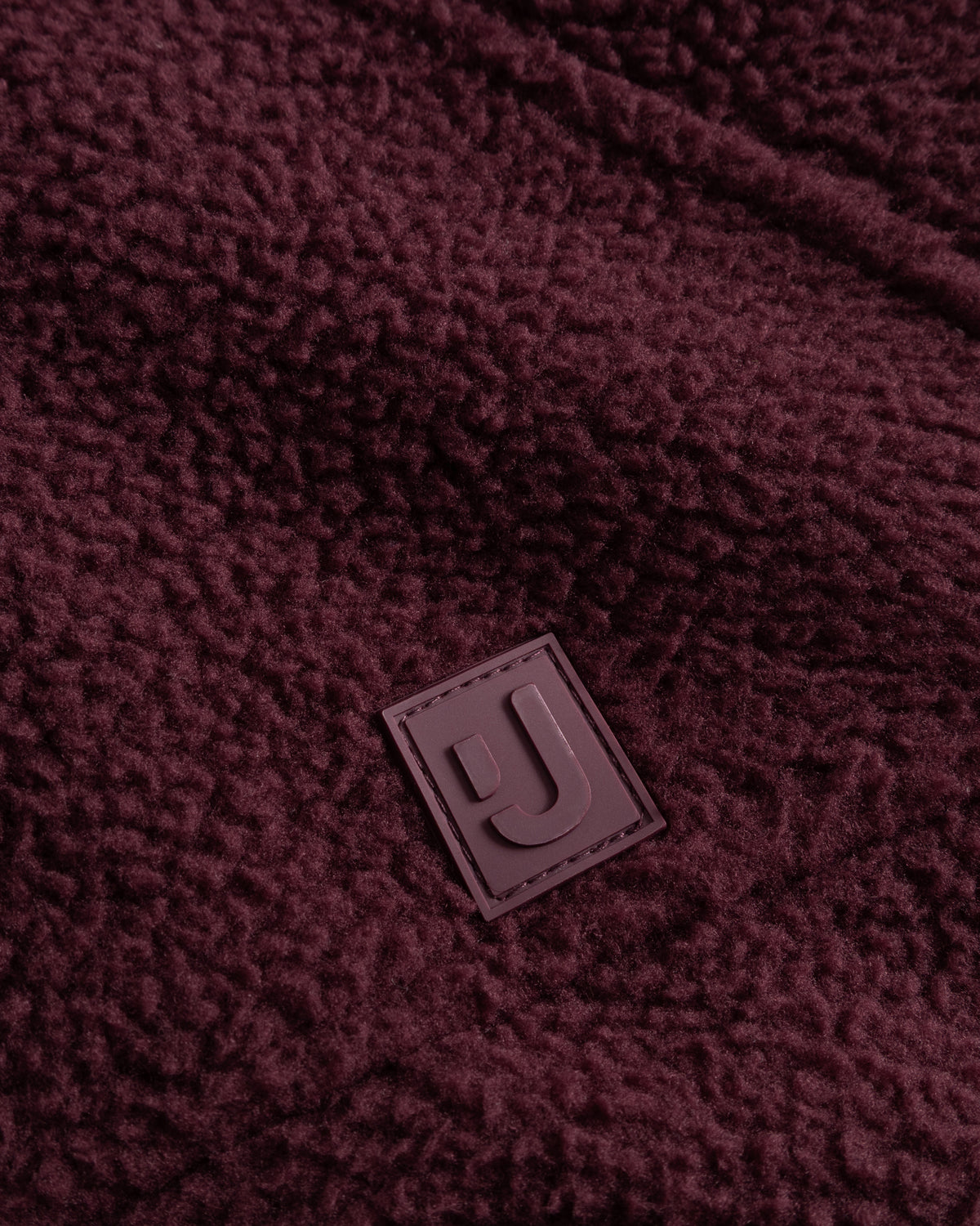 Unsere hochwertiges Logo-Badge auf der Fleecejacke Nova in Burgunderrot.  