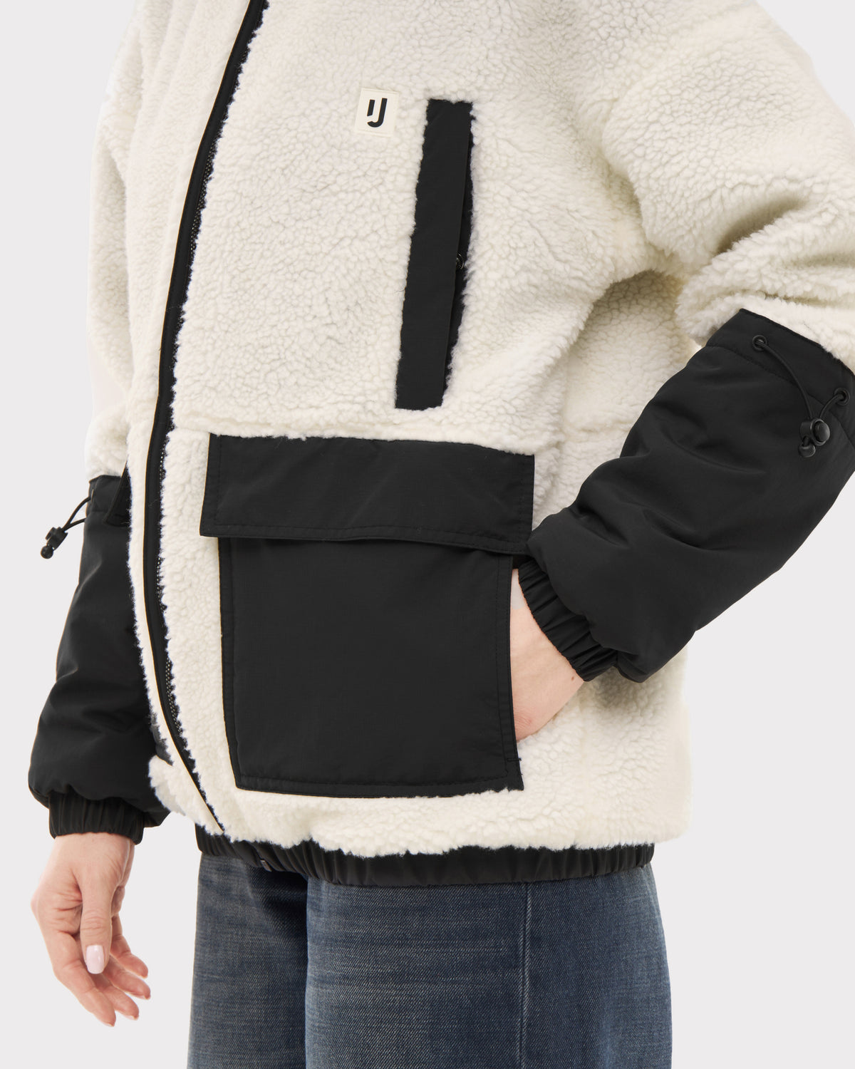 Teddy Fleecejacke 'Carson' in Creme mit schwarzen Akzenten und Taschen, an einem Mann mit Jeans