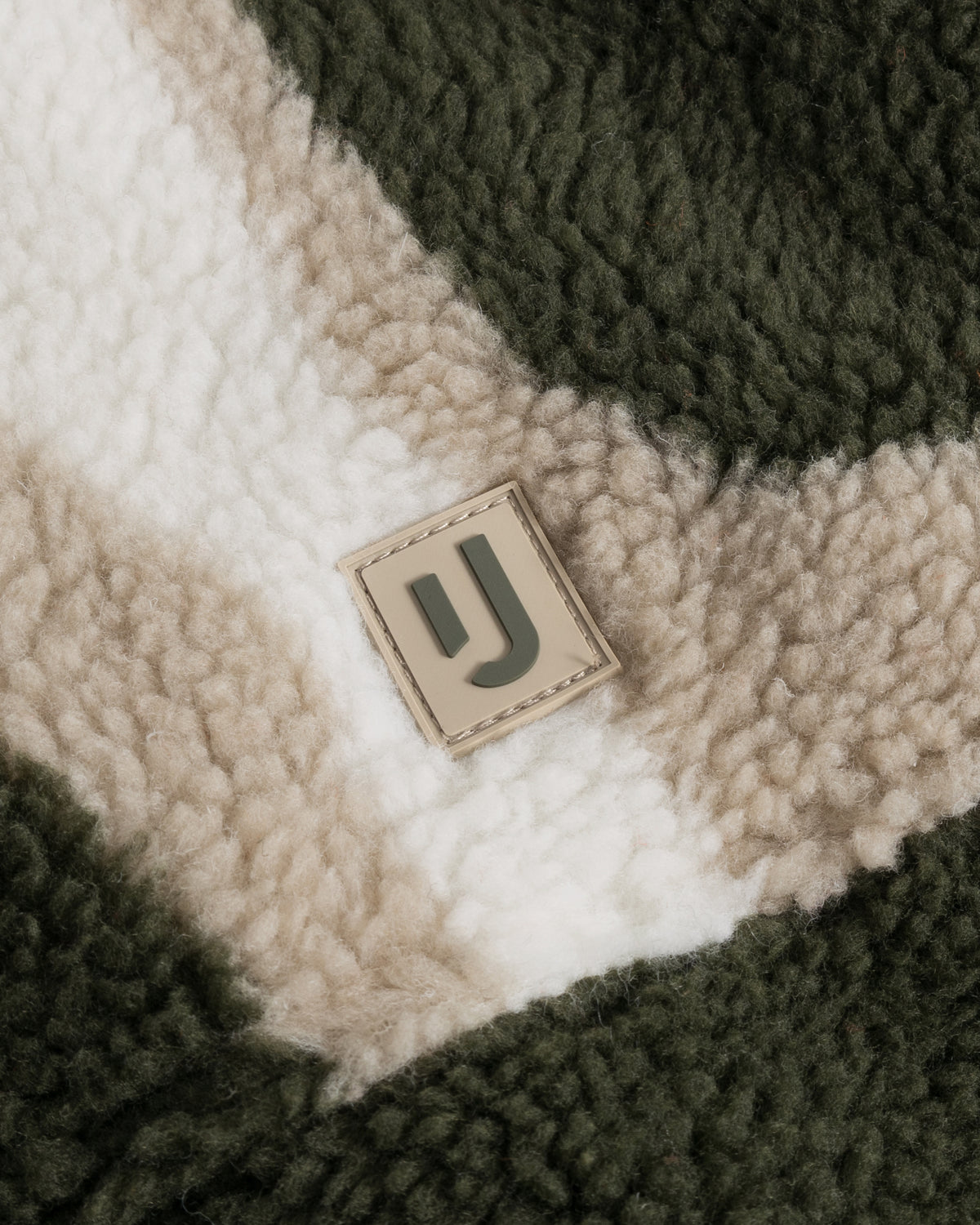 Nahaufnahme der Teddy Fleeceweste "Bryson" mit olivefarbenem und beigem Muster und Johnny Urban Logo