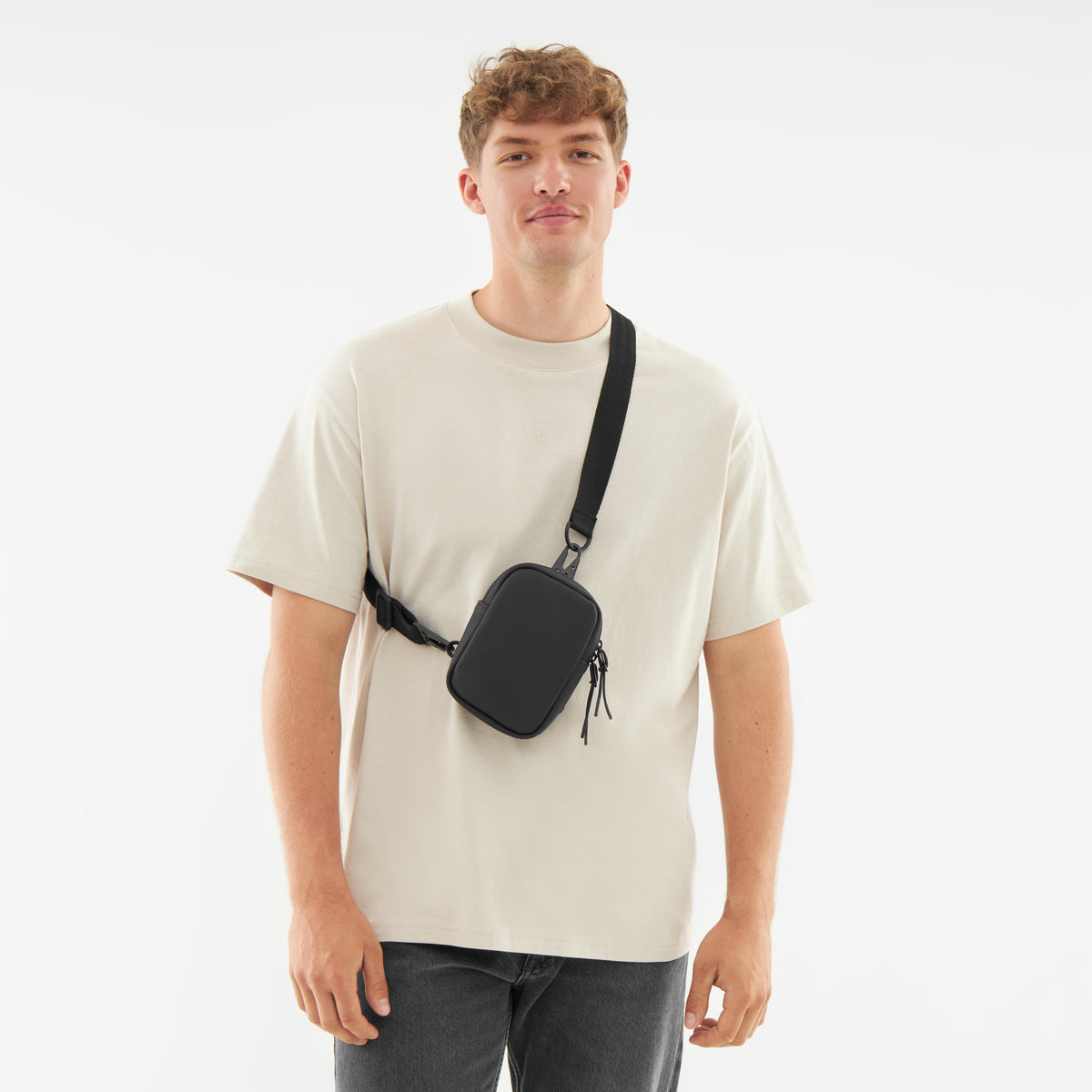 Mann trägt schwarzen Front Pack 'Toby' quer über die Brust, helles T-Shirt, dunkle Jeans