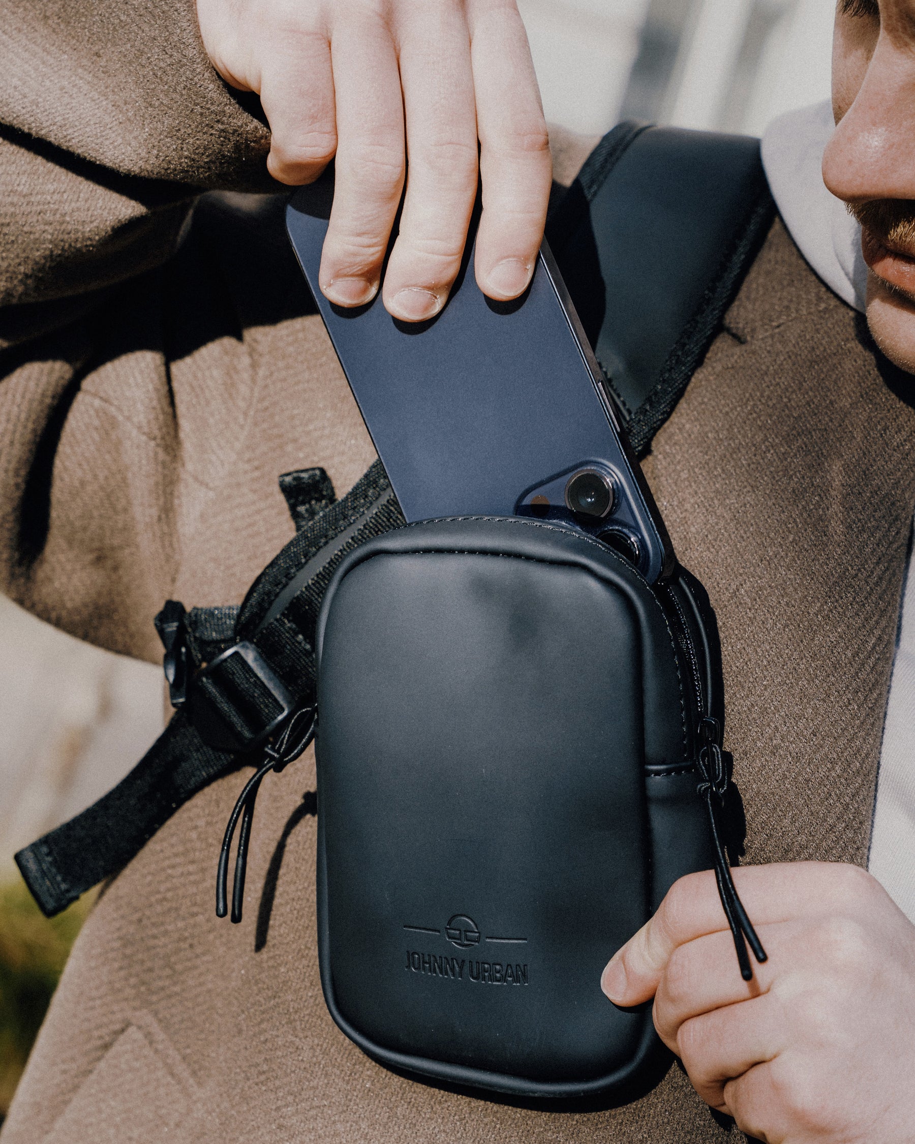 Person steckt ein Smartphone in das schwarze Front Pack 'Toby' von Johnny Urban