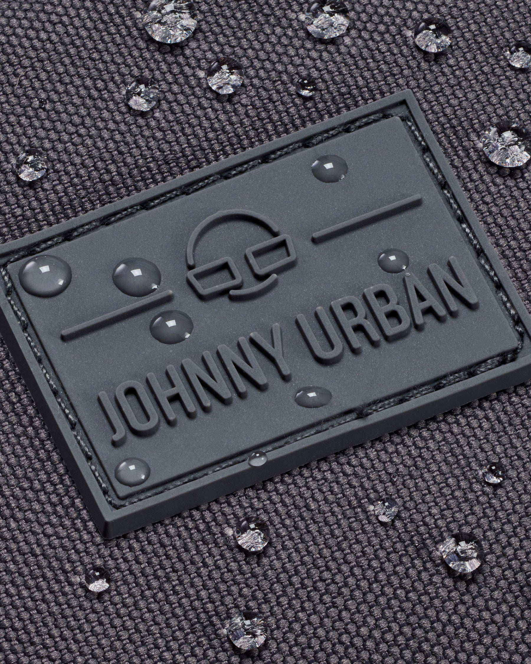 Nahe Aufnahme des wasserdichten, dunkelgrauen Materials der Bauchtasche 'Erik Large' von Johnny Urban mit Logo und Wassertropfen