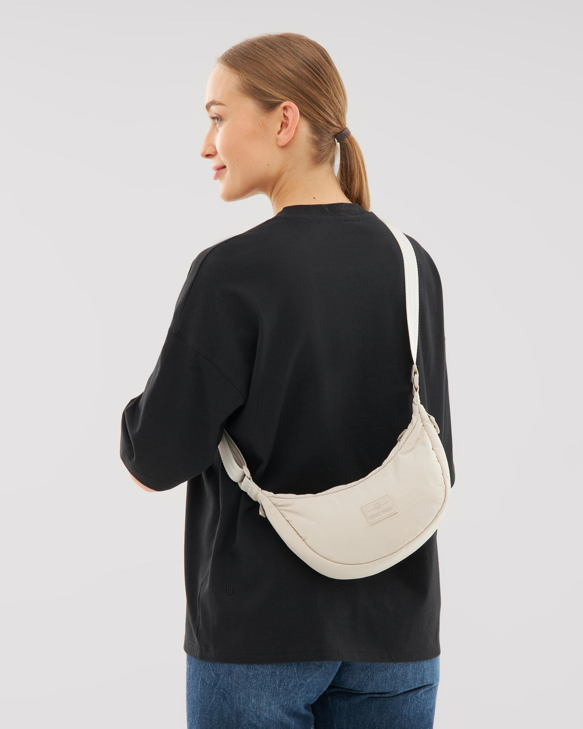 Frau von hinten mit schwarzem Sweatshirt und Jeans trägt beige Half Moon Bag 'Kaia Small' über die Schulter