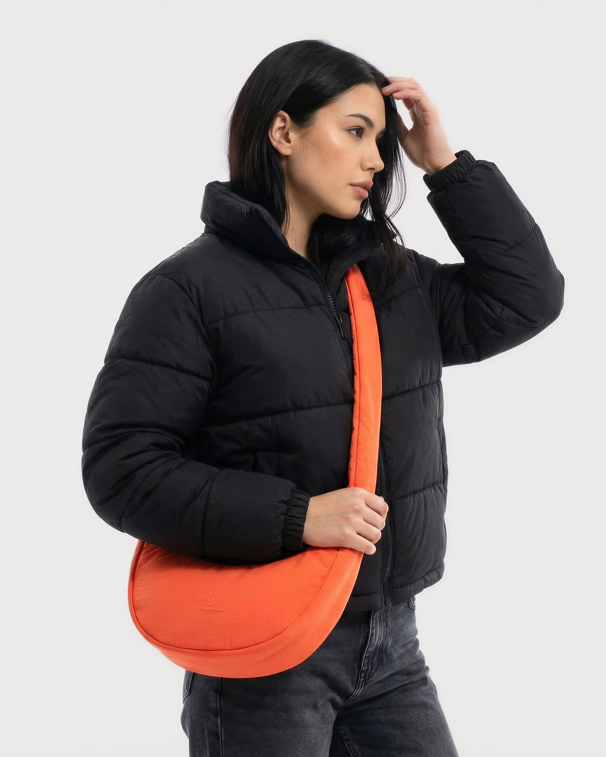 Unser weibliches Model zeigt sich hier mit der Johnny Urban Half-Moon-Bag "Lou Medium" in coral-rot. | KI generiertes Bild