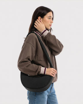 Unser weibliches Model zeigt sich hier mit der Johnny Urban Half-Moon-Bag "Lou Medium" in schwarz. | KI generiertes Bild