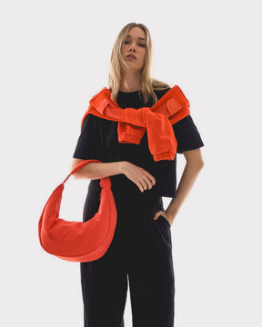Unser weibliches Model präsentiert sich hier mit der Half-Moon-Bag "Lou Large" in corla-rot. 