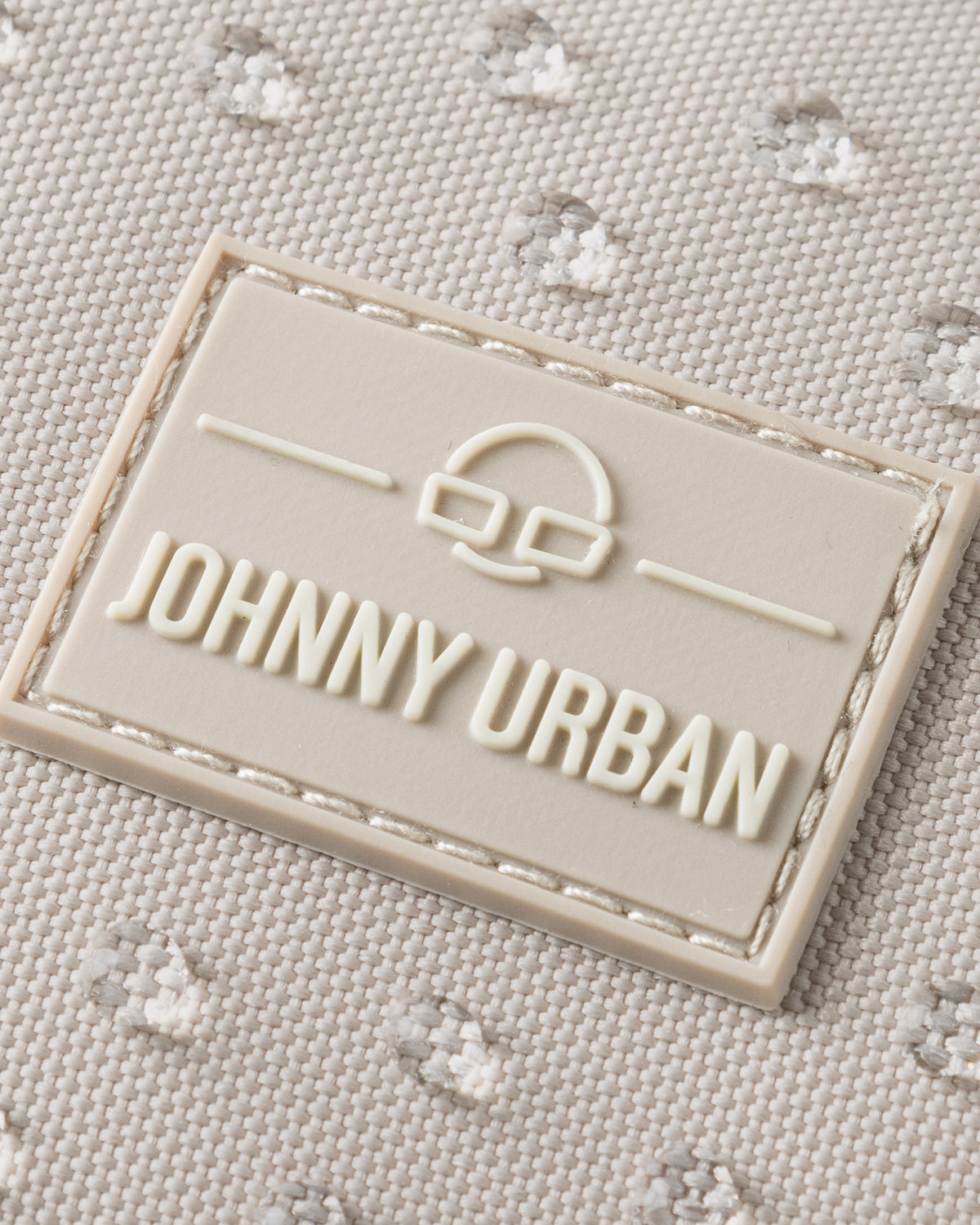 Nahaufnahme des Johnny Urban Logos auf sandfarbenem, wasserabweisendem Stoff mit kleiner Punktstruktur