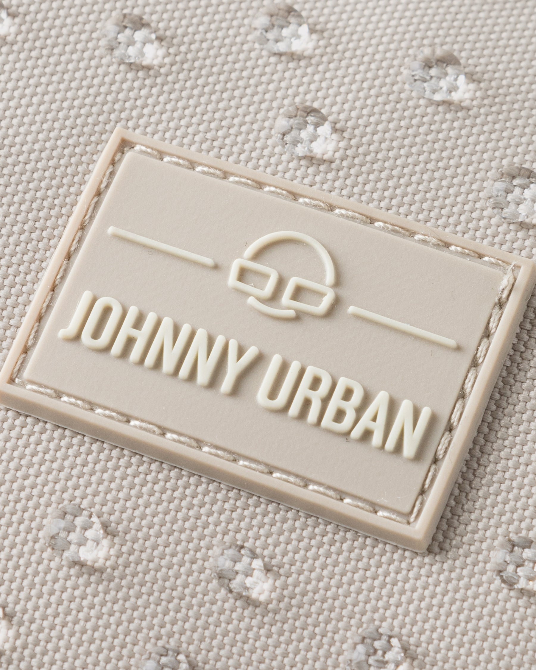 Nahaufnahme des Johnny Urban Logos auf sandfarbenem, wasserabweisendem Stoff mit kleiner Punktstruktur